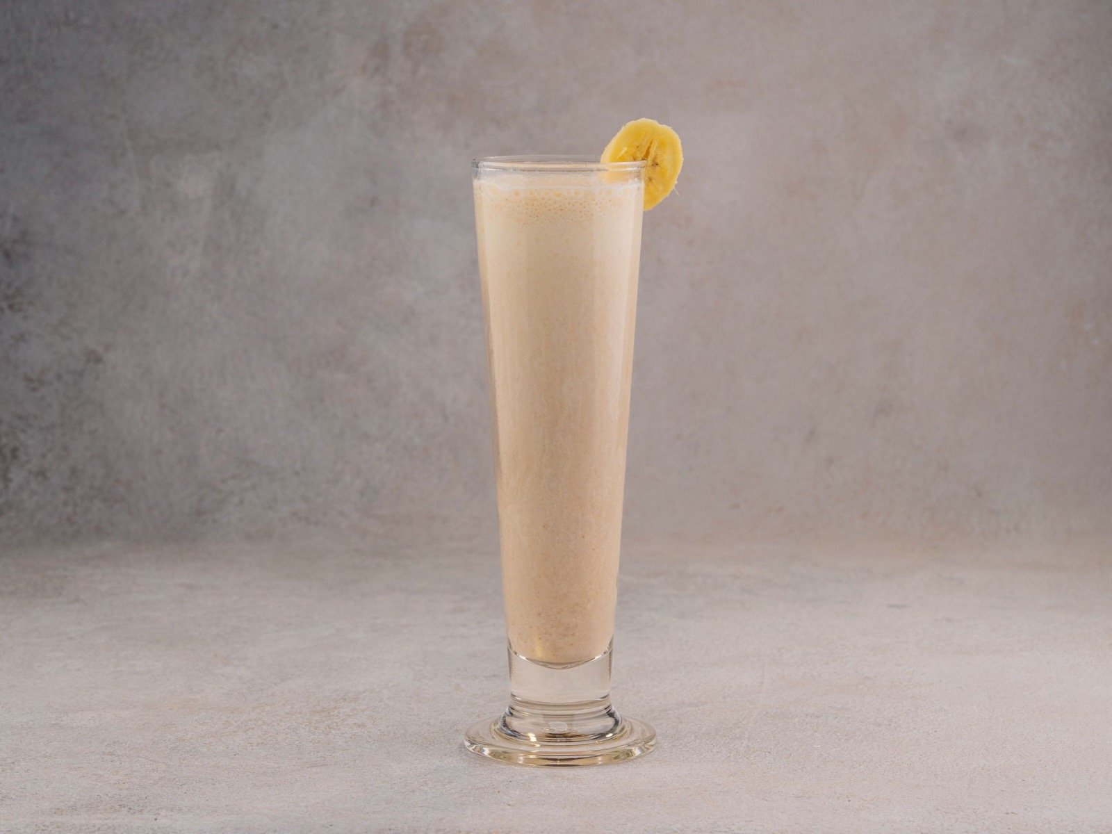Bicchiere alto con frullato proteico color crema, guarnito con una fetta di banana, la fase liquida del recupero dopo chirurgia ortognatica a Caserta e Napoli